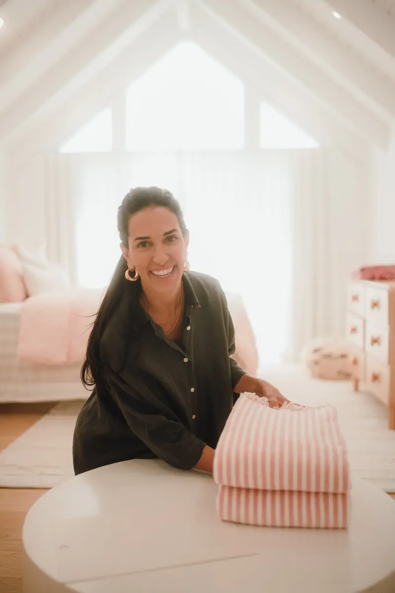 Ive Bitencourt folding pink striped linen in a bright, organised kids' bedroom
