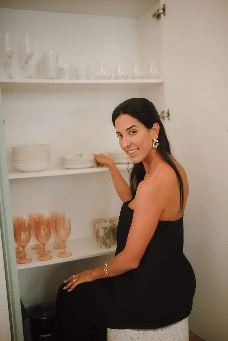 Ive Bitencourt arranging plates and glassware in a neatly organised kitchen cupboard